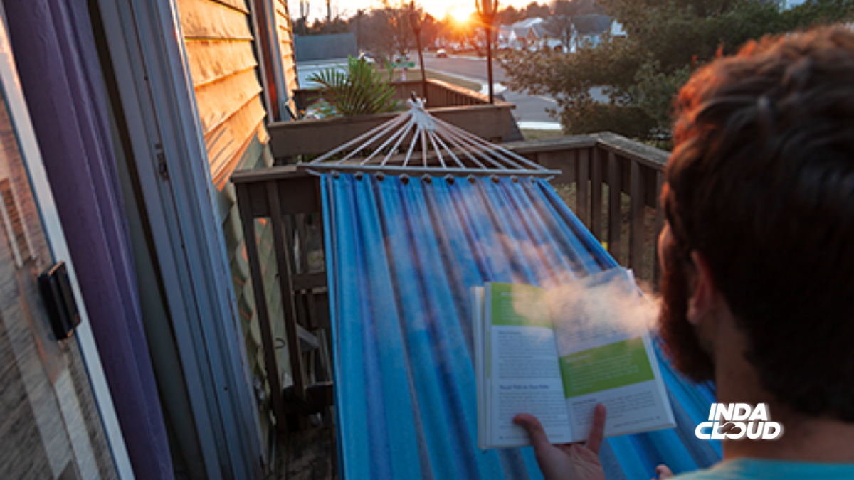 Person relaxing on a hammock, reading a book while exhaling vapor, with a sunset in the background.